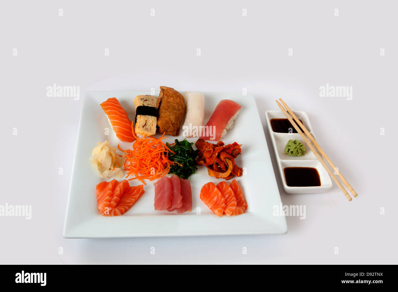 Assortiment de sushi et sashimi sur une plaque carrée blanche avec des baguettes Banque D'Images