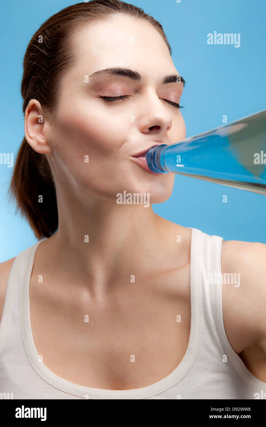 Une jeune femme à boire le contenu de l'eau d'une bouteille d'eau en verre Banque D'Images