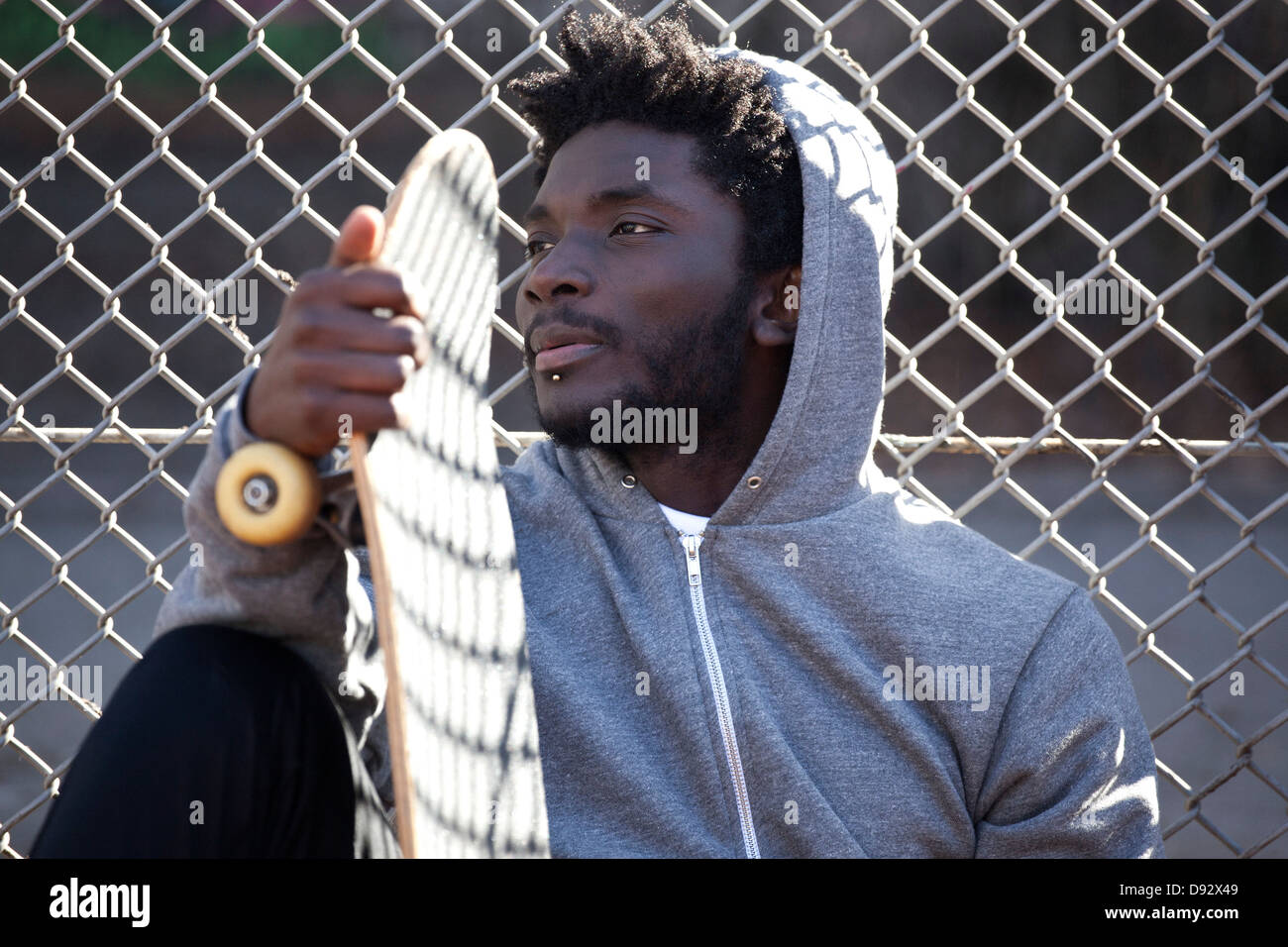Un jeune homme appuyé contre une clôture de la tenue d'un skateboard Banque D'Images