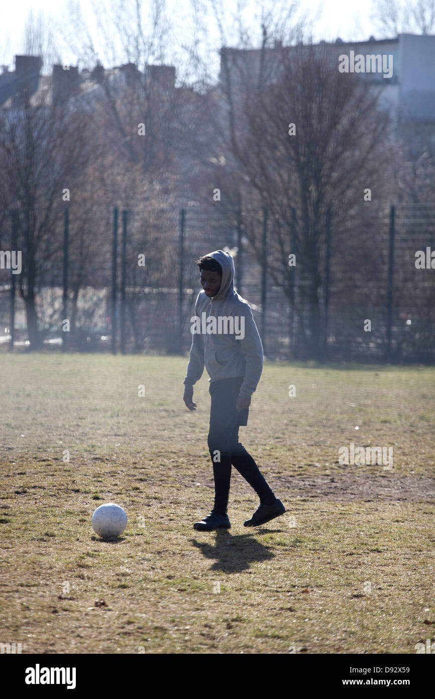 Un jeune homme botter un ballon de soccer dans un parc de la ville Banque D'Images