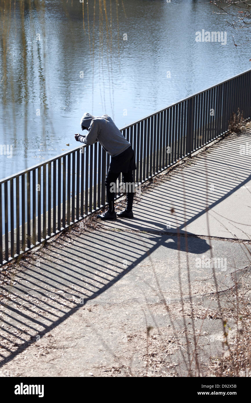 Un jeune homme appuyé contre une rambarde regardant une rivière Banque D'Images
