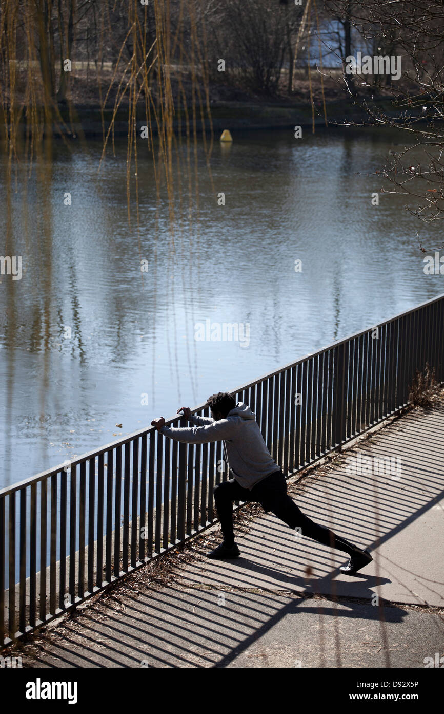 Un homme faisant un mouvement brusque étirement contre une rambarde près d'une rivière Banque D'Images