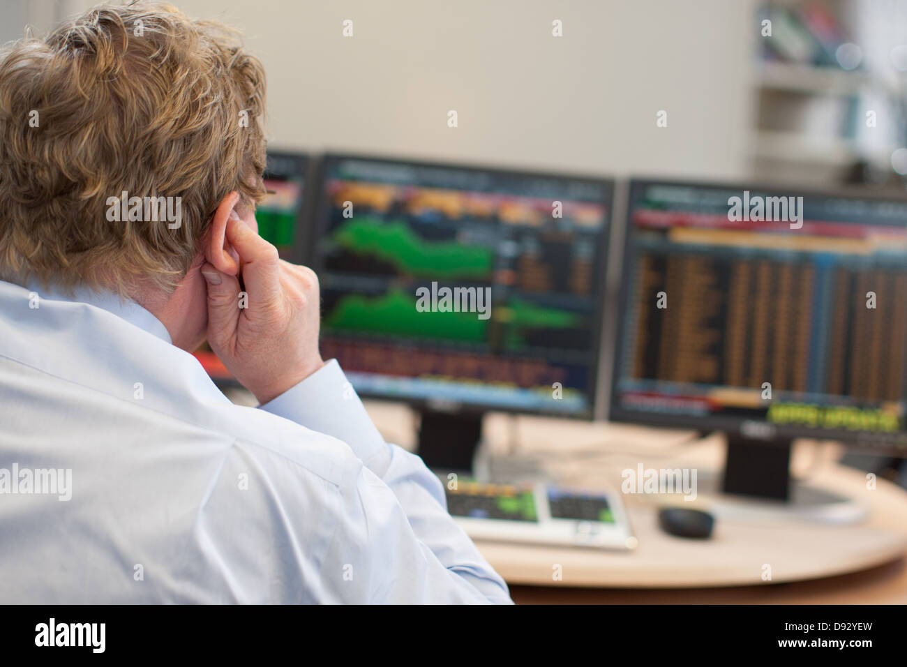 Courtier en valeurs à son bureau bureau avec bourse et cotations boursières sur les écrans d'ordinateurs et des journaux financiers Banque D'Images