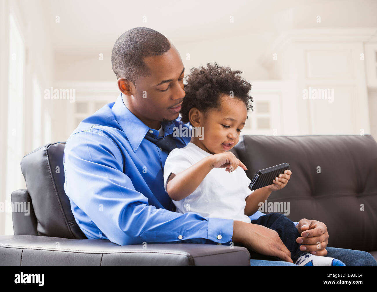 Père et fils jouant avec cell phone on sofa Banque D'Images