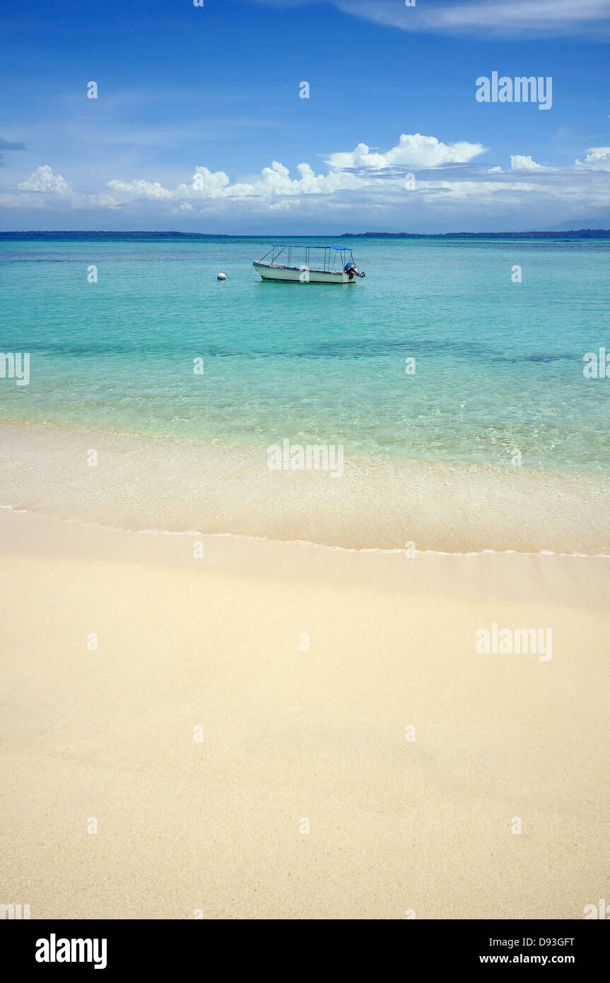 La plage de sable tropicale à l'eau claire et d'un bateau seul dans la mer des Caraïbes Banque D'Images