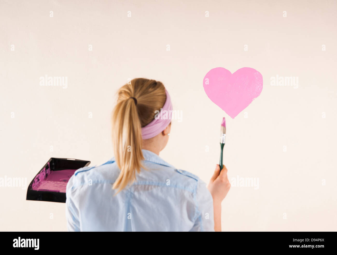 Studio Shot of Young Woman Painting Heart on Wall Banque D'Images
