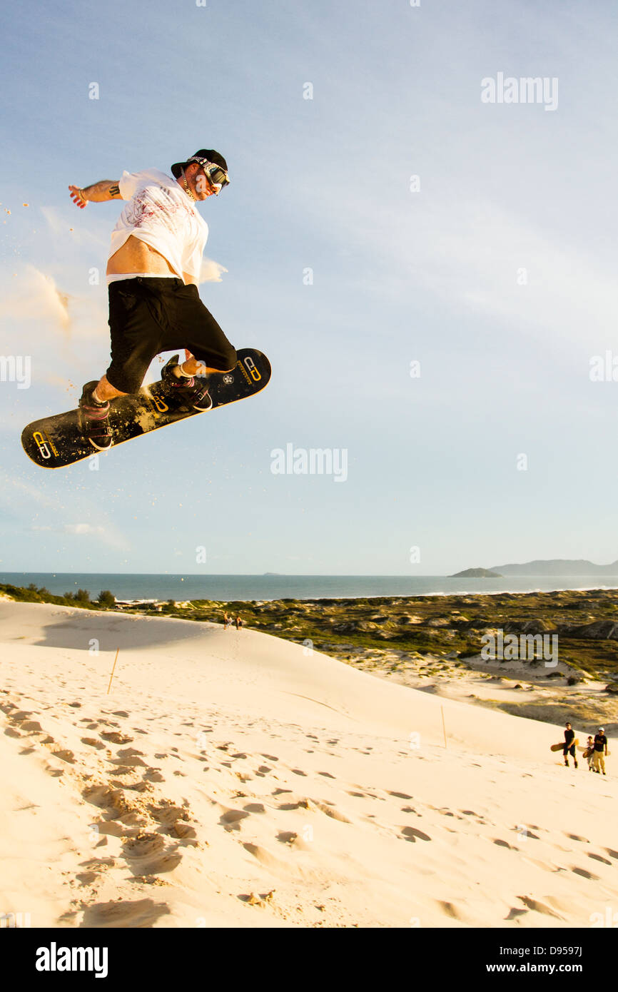 Sandboarder jumping and holding sa board sur les dunes de Joaquina Plage. Banque D'Images