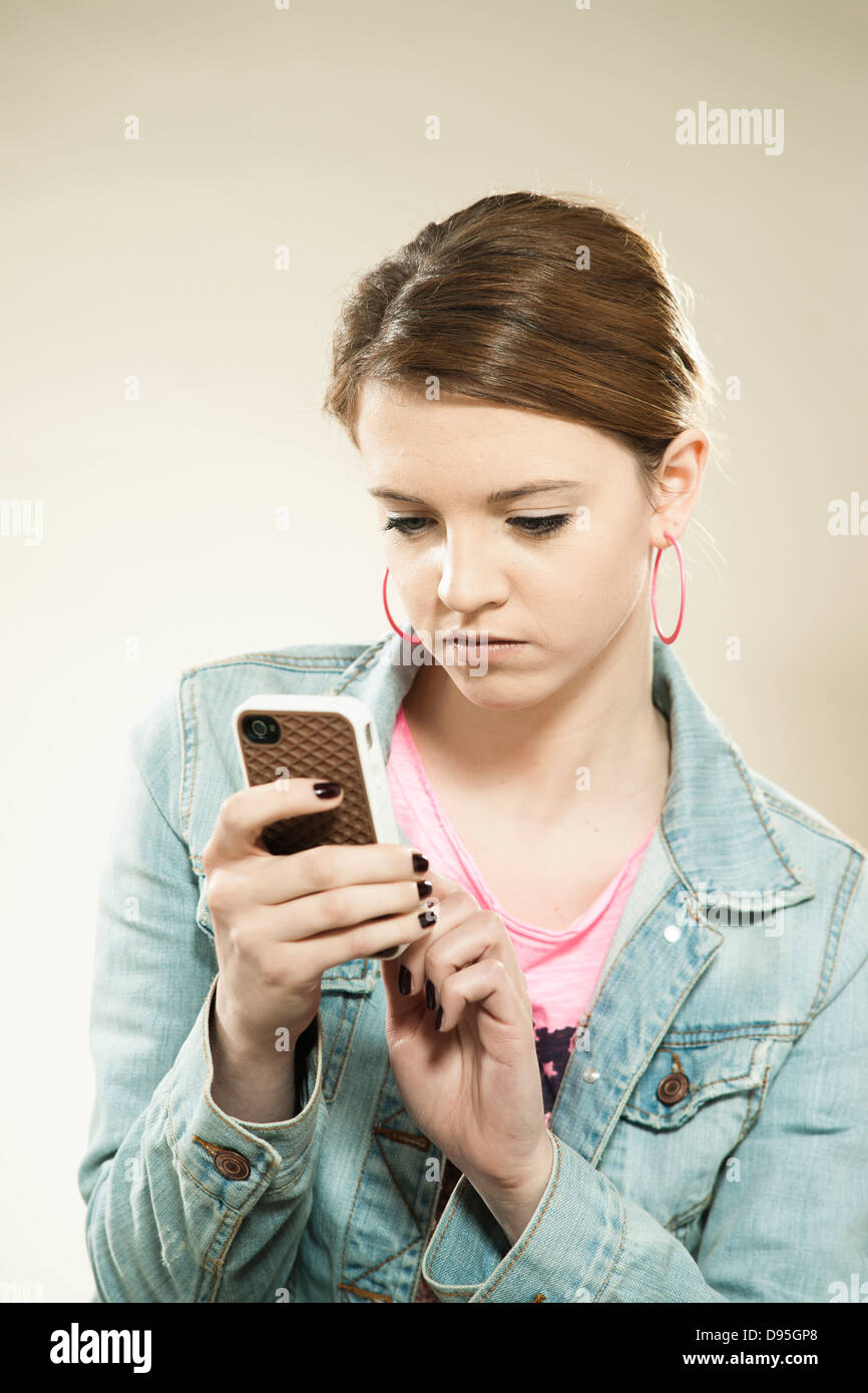 Portrait of Teenage Girl Reading Text Message on a Cell Phone in Studio Banque D'Images