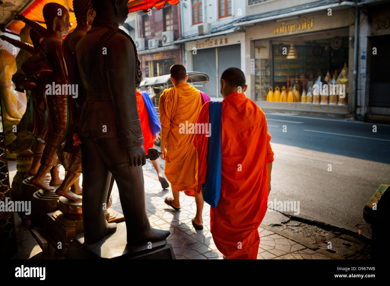Moines en passant devant un assortiment de personnages religieux et de statues au coeur de Bangkok, dédiée à la fabrication de statues Banque D'Images