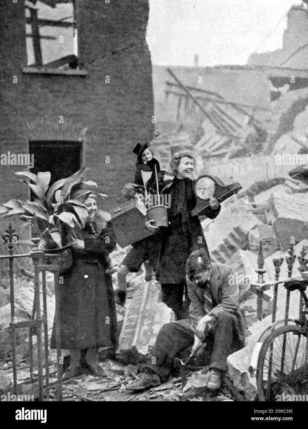 Les Londoniens sans abri par un raid de bombardement allemand pendant le Blitz de 1940 holding certains biens précieux récupérés dans les ruines et mettre sur brave, visages de sourire : octobre 1940. La Seconde Guerre mondiale. Banque D'Images