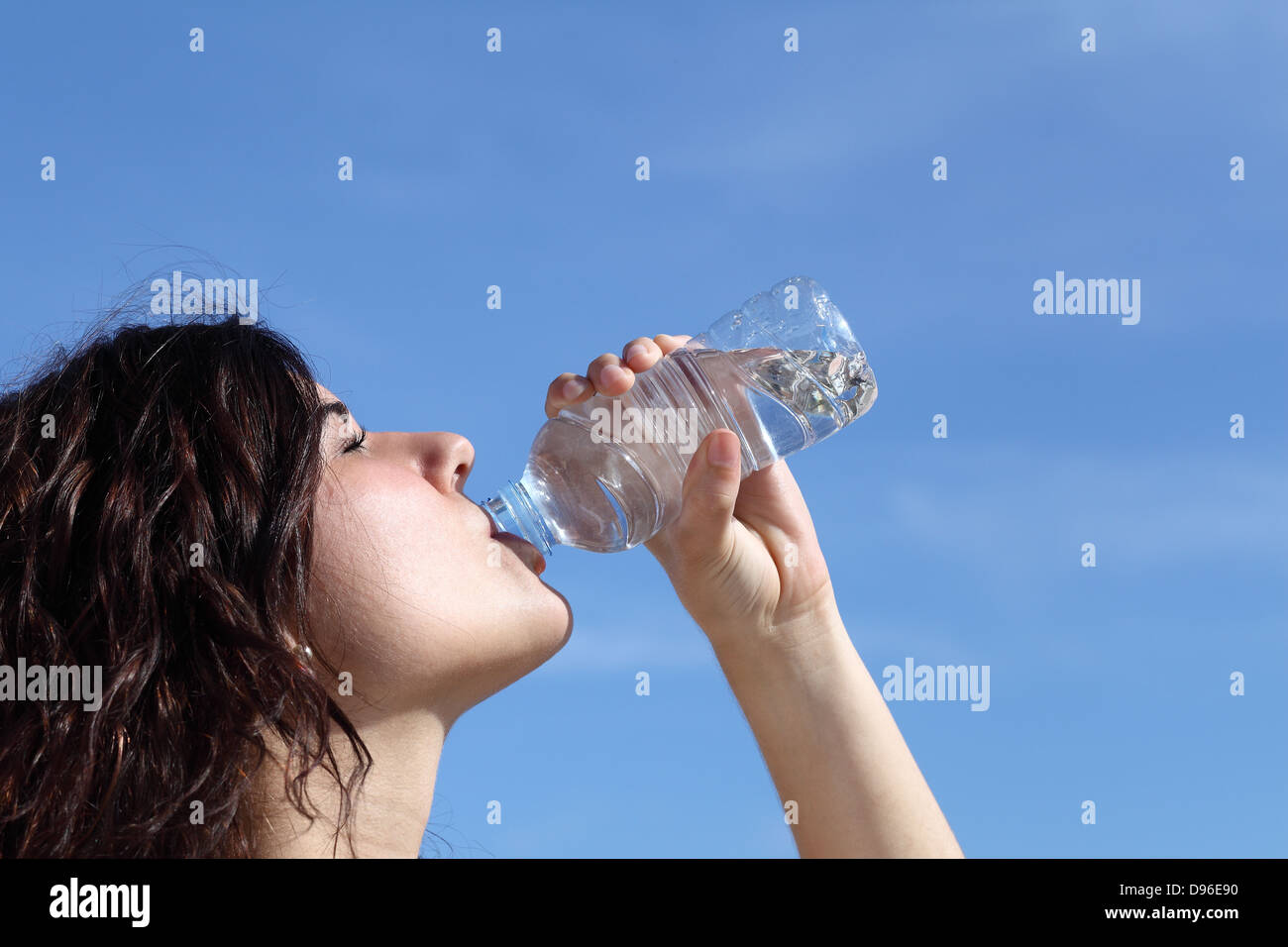 Profil d'une belle femme l'eau potable à partir d'une bouteille en plastique avec un ciel bleu en arrière-plan Banque D'Images