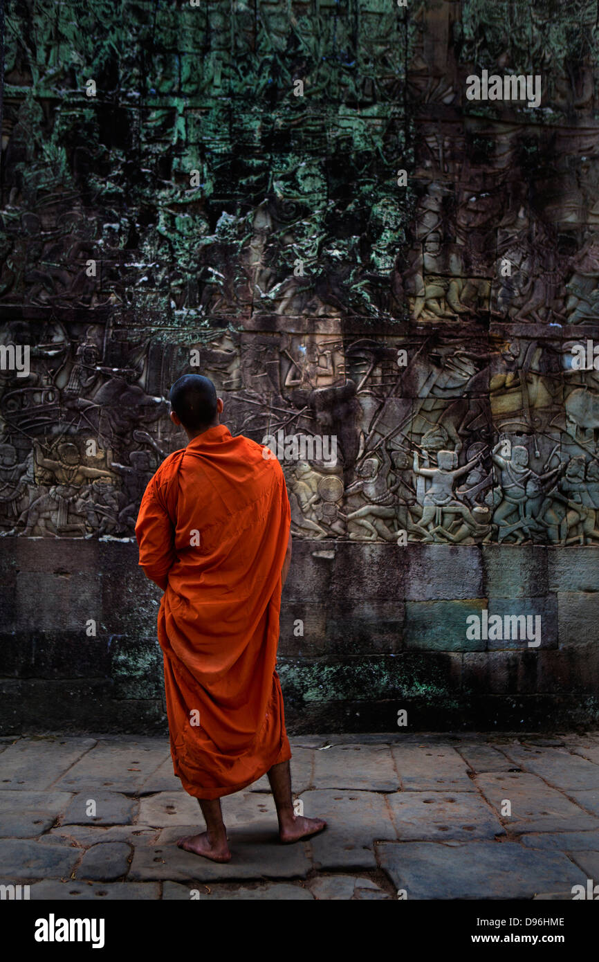 Le moine bouddhiste à la recherche à bas-reliefs sur le mur extérieur de la galerie extérieure du temple Bayon, Angkor, Cambodge Banque D'Images