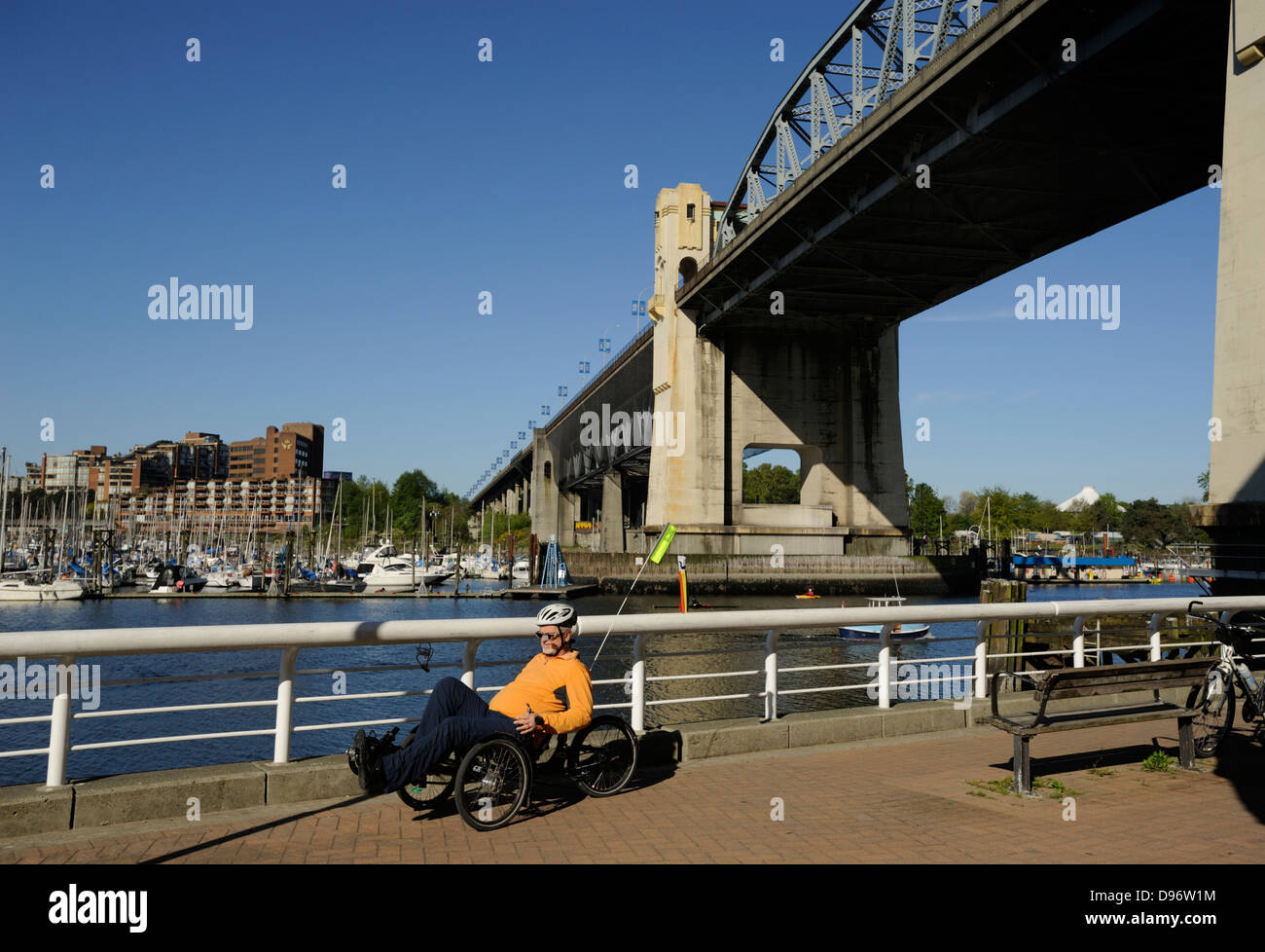 Homme monté sur un vélo couché le long de False Creek seawall promenade avec pont de la rue Burrard, Vancouver (C.-B.) ci-dessus Banque D'Images