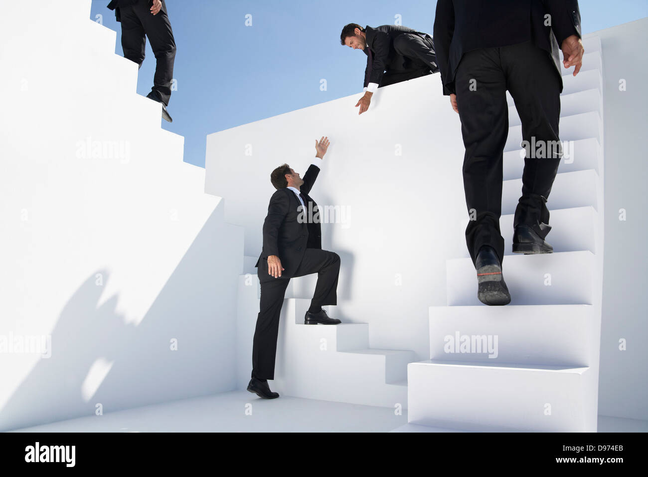 Les hommes d'affaires à monter des escaliers, se déplaçant vers le bas et de les aider à monter un autre homme Banque D'Images