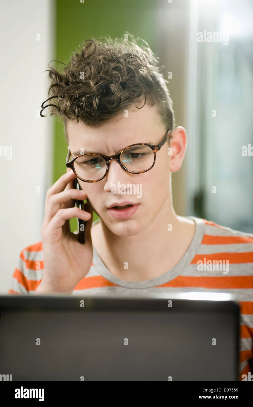 Germany, Bavaria, Munich, Young man talking on mobile phone and using laptop in cafe Banque D'Images