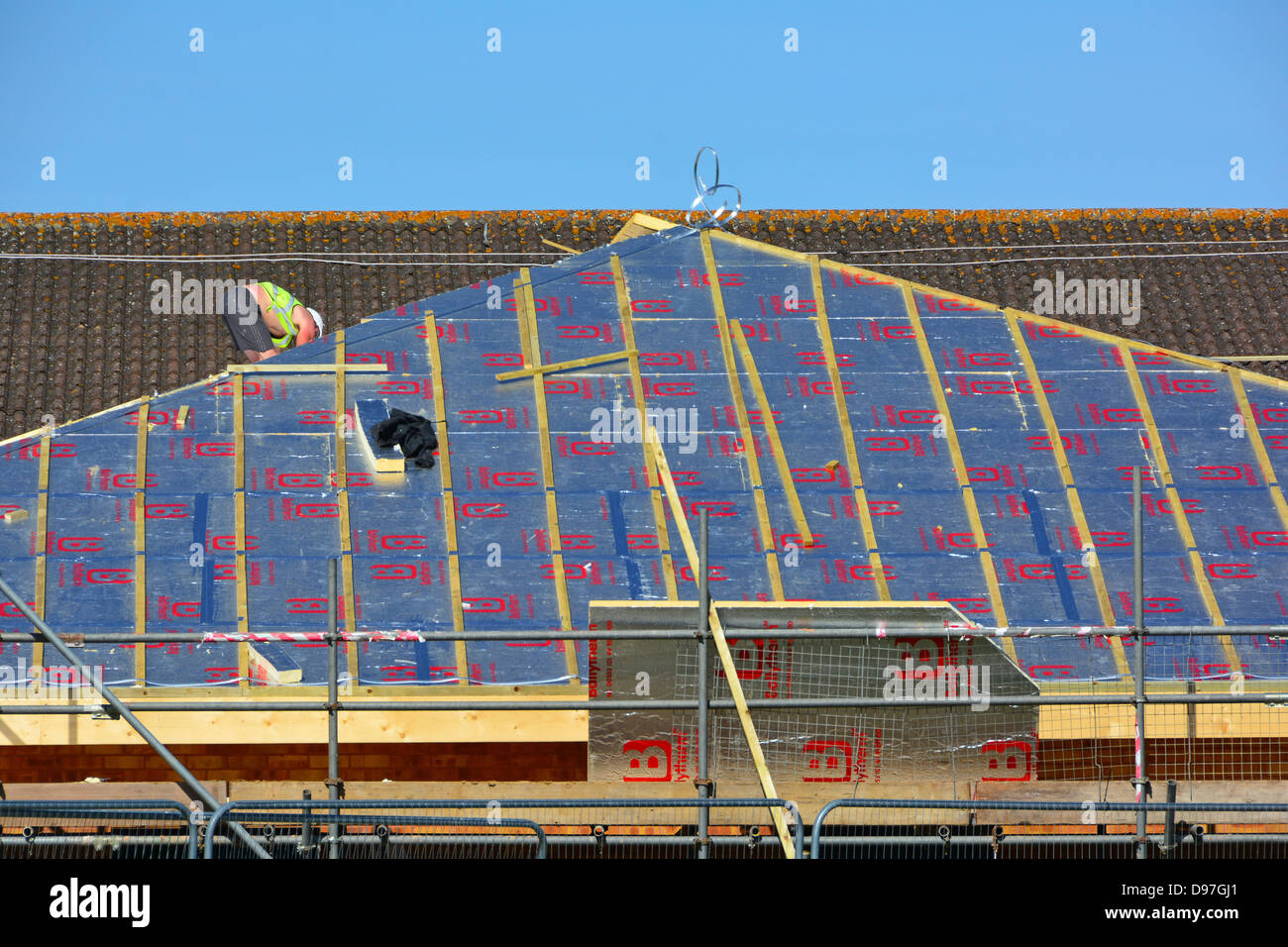 Échafaudage sur le chantier de construction et ouvrier de fixation avec support en feuille Isolation en mousse à économie d'énergie sur le toit incliné de l'extension scolaire Essex Angleterre Royaume-Uni Banque D'Images