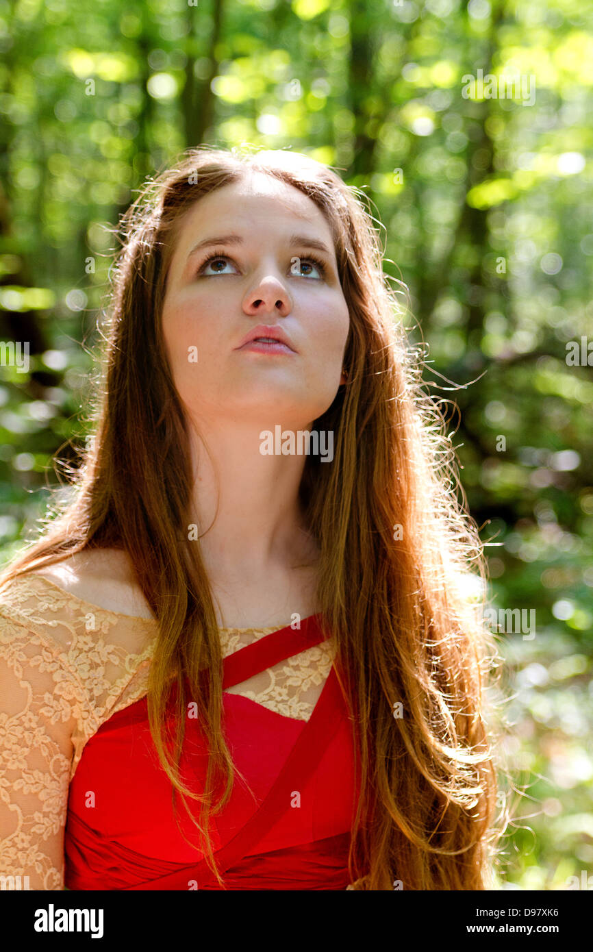 Jeune femme aux cheveux brun-doré et rouge robe médiévale avec accents se trouve dans la forêt, regardant imploringly Banque D'Images