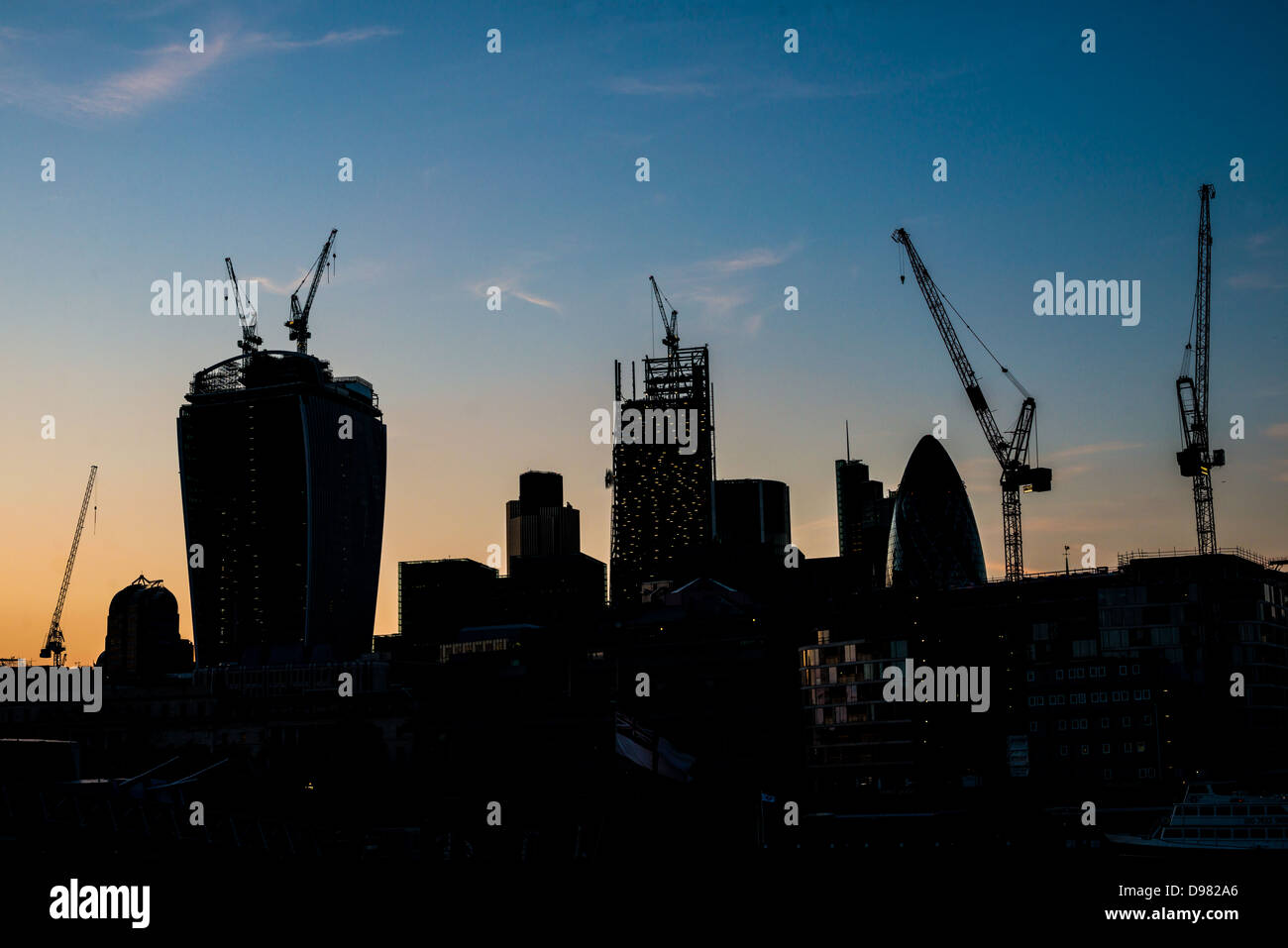 London Skyline construction grues Silhouette Londres // LONDRES, Royaume-Uni — L'horizon en évolution de Londres se silhouette de façon spectaculaire dans un ciel sombre, mettant en valeur la construction en cours de nouveaux gratte-ciel. Cette image saisissante reflète la croissance dynamique et l'ambition architecturale de la ville, avec les contours des immeubles en hauteur émergeants qui côtoient des monuments établis, symbolisant la transformation continue de Londres en tant que centre financier et culturel mondial. Banque D'Images