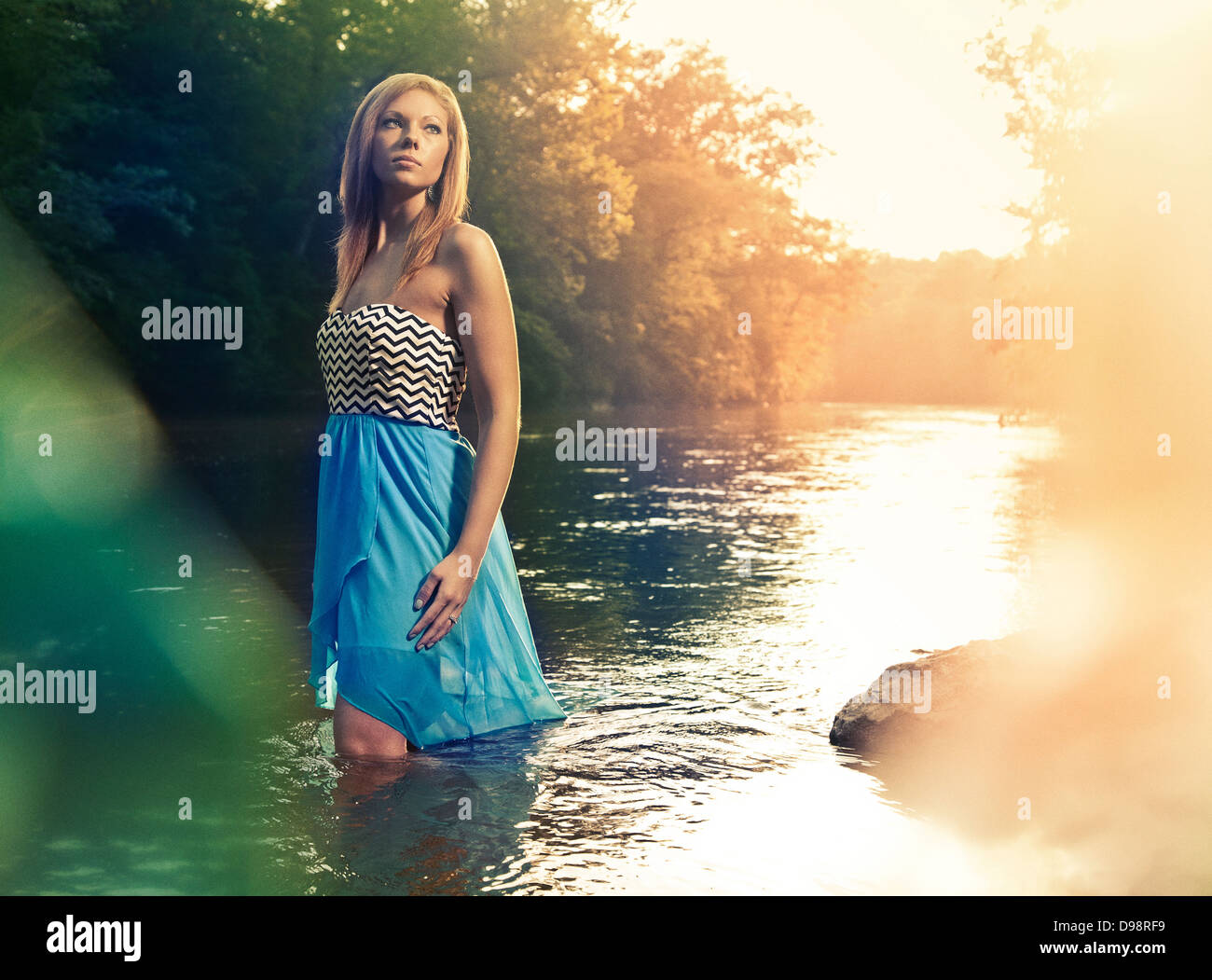 Femme en robe bleue walking in river pendant le coucher du soleil Banque D'Images