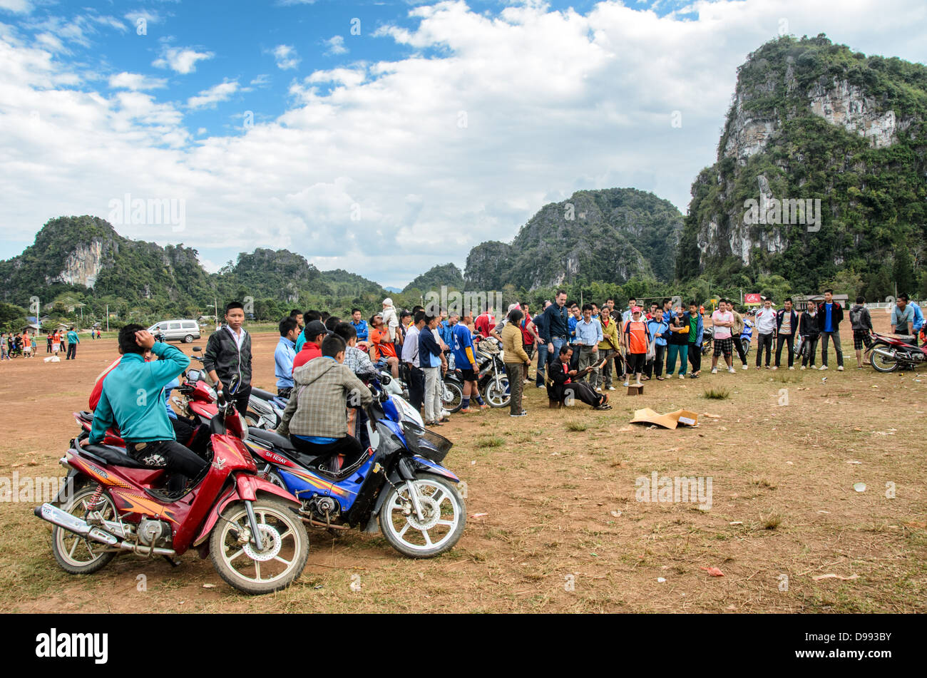 VIENG Xai, Laos — les étudiants spectateurs s'alignent sur leurs scooters et leurs vélos pour assister à un concours d'arbalètes sur un terrain de jeu en terre battue parmi le terrain accidenté près de Vieng Xai dans le nord-est du Laos. L’événement local attire des participants et des spectateurs des villages environnants de cette région rurale. Banque D'Images