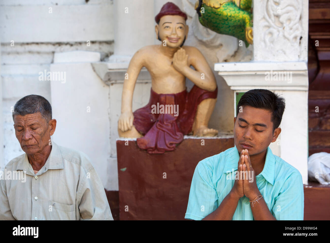 Deux hommes, les yeux clos, s'asseoir sur le sol en marbre et de prier à la temple Schwedagon à Yangon (Rangoon). figures sculptées. Banque D'Images