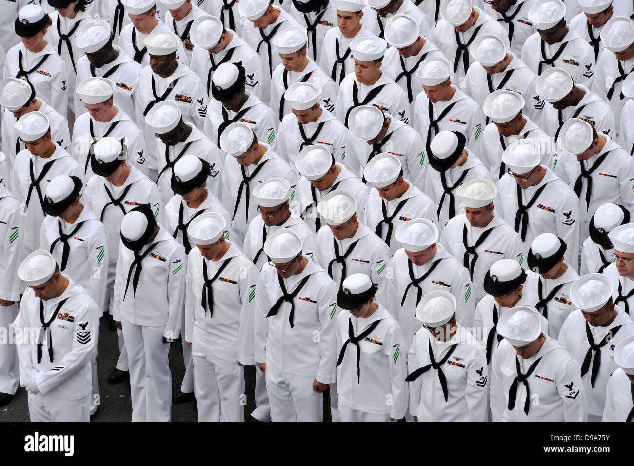 Les marins de l'US Navy affecté à l'assaut amphibie USS Makin Island baissent la tête pour l'appel au cours d'une cérémonie de passation de commandement tenue sur le pont d'envol du navire le 14 juin 2013 à San Diego, CA. Banque D'Images