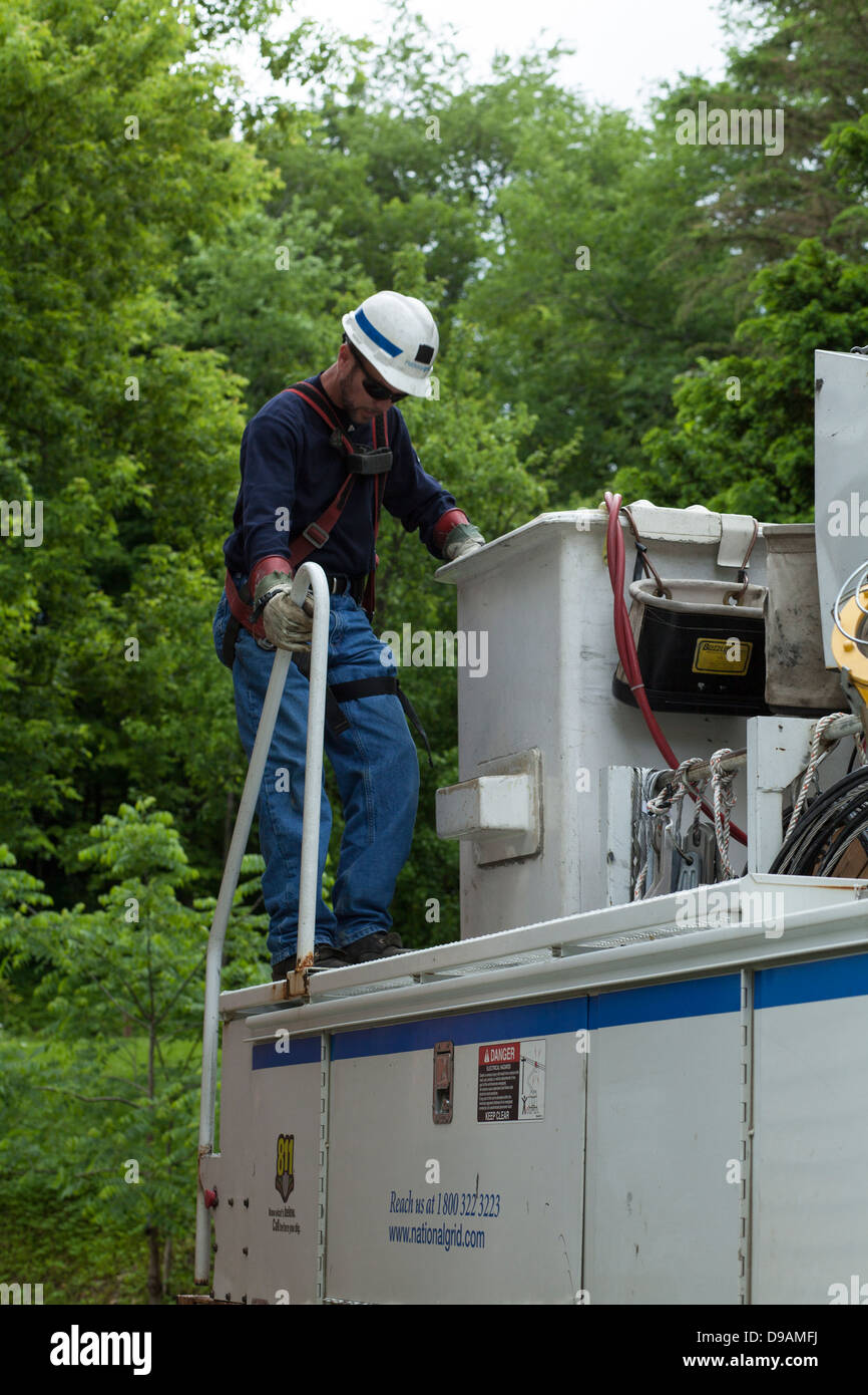 Une compagnie d'électricité Workman est l'escalade en grue sur son camion pour envelopper une ligne électrique pour protéger les autres travailleurs. Banque D'Images