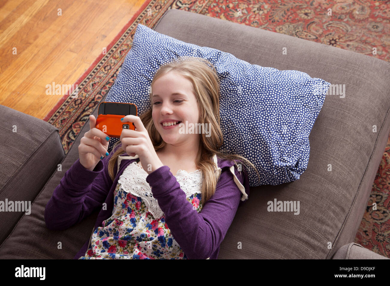 Girl lying on sofa playing handheld video game Banque D'Images