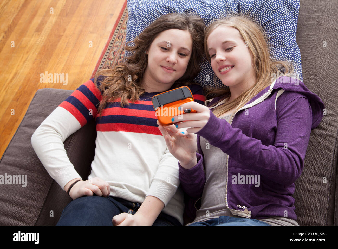 Girls lying on sofa playing handheld video game Banque D'Images