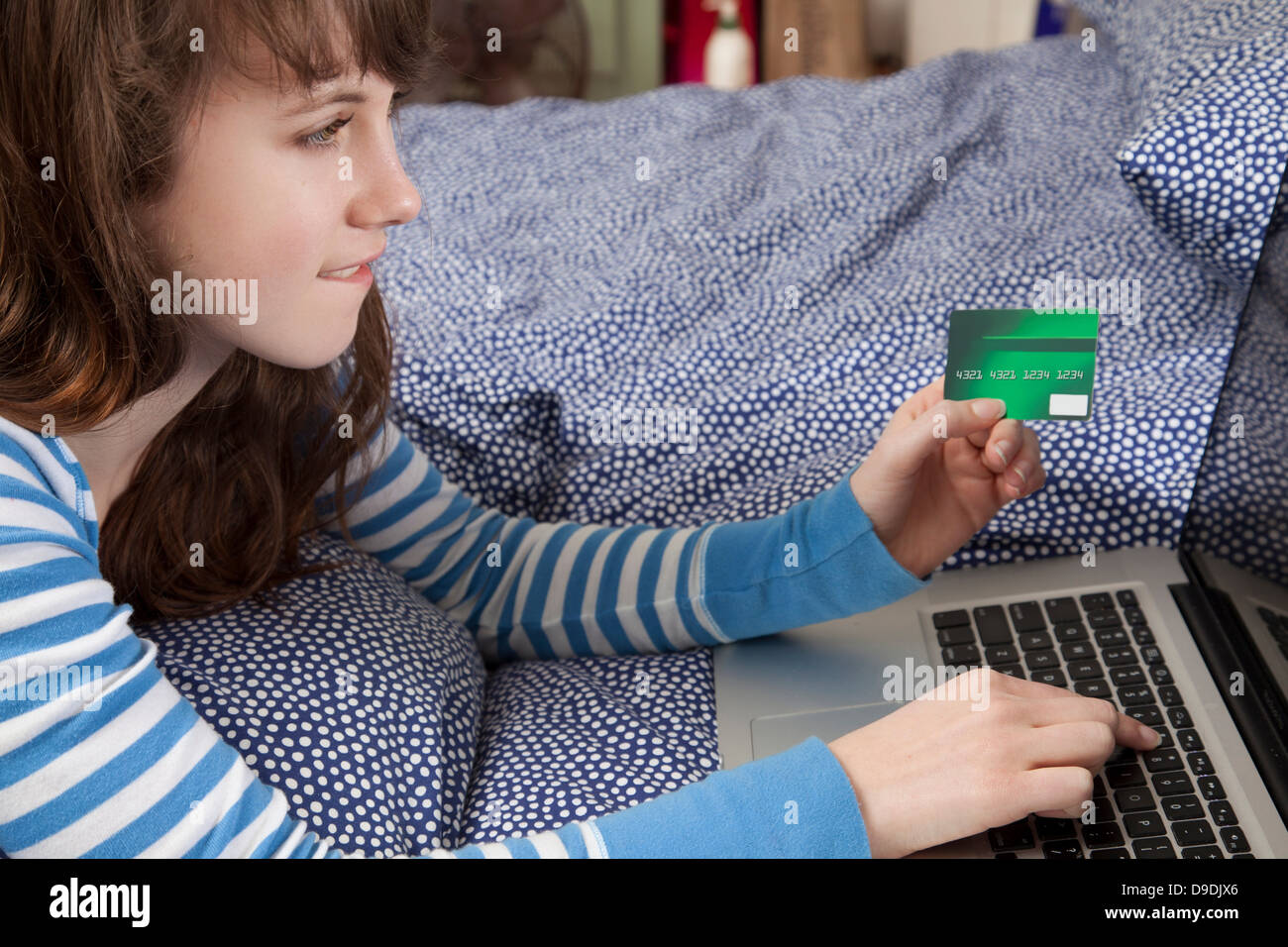 Girl lying on bed with laptop internet shopping Banque D'Images