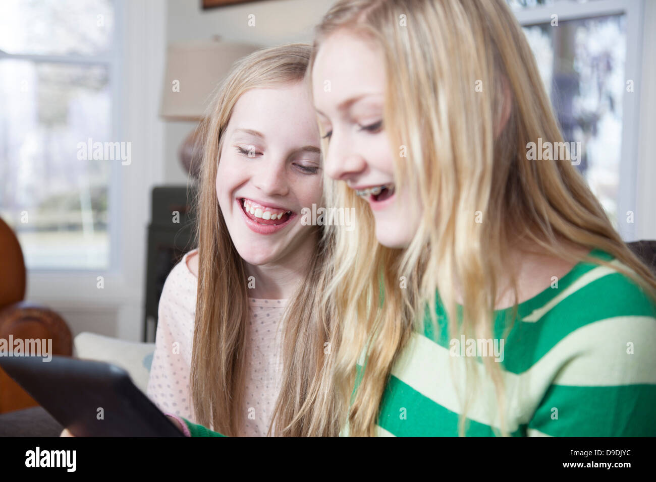 Girls sitting on sofa looking at digital tablet Banque D'Images