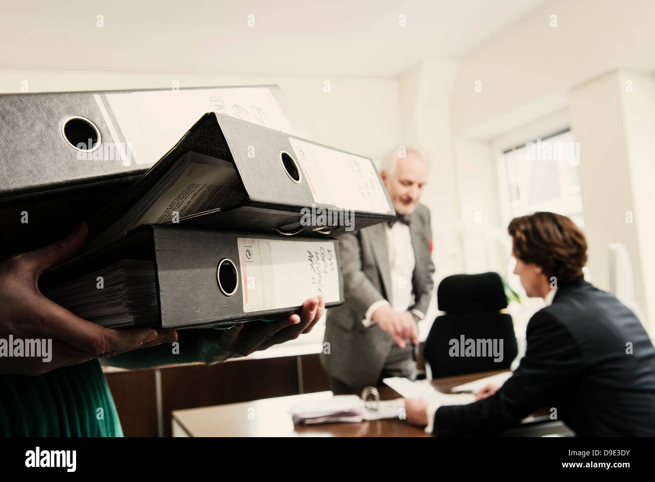 Femme transportant les reliures à anneaux, les hommes en arrière-plan Banque D'Images