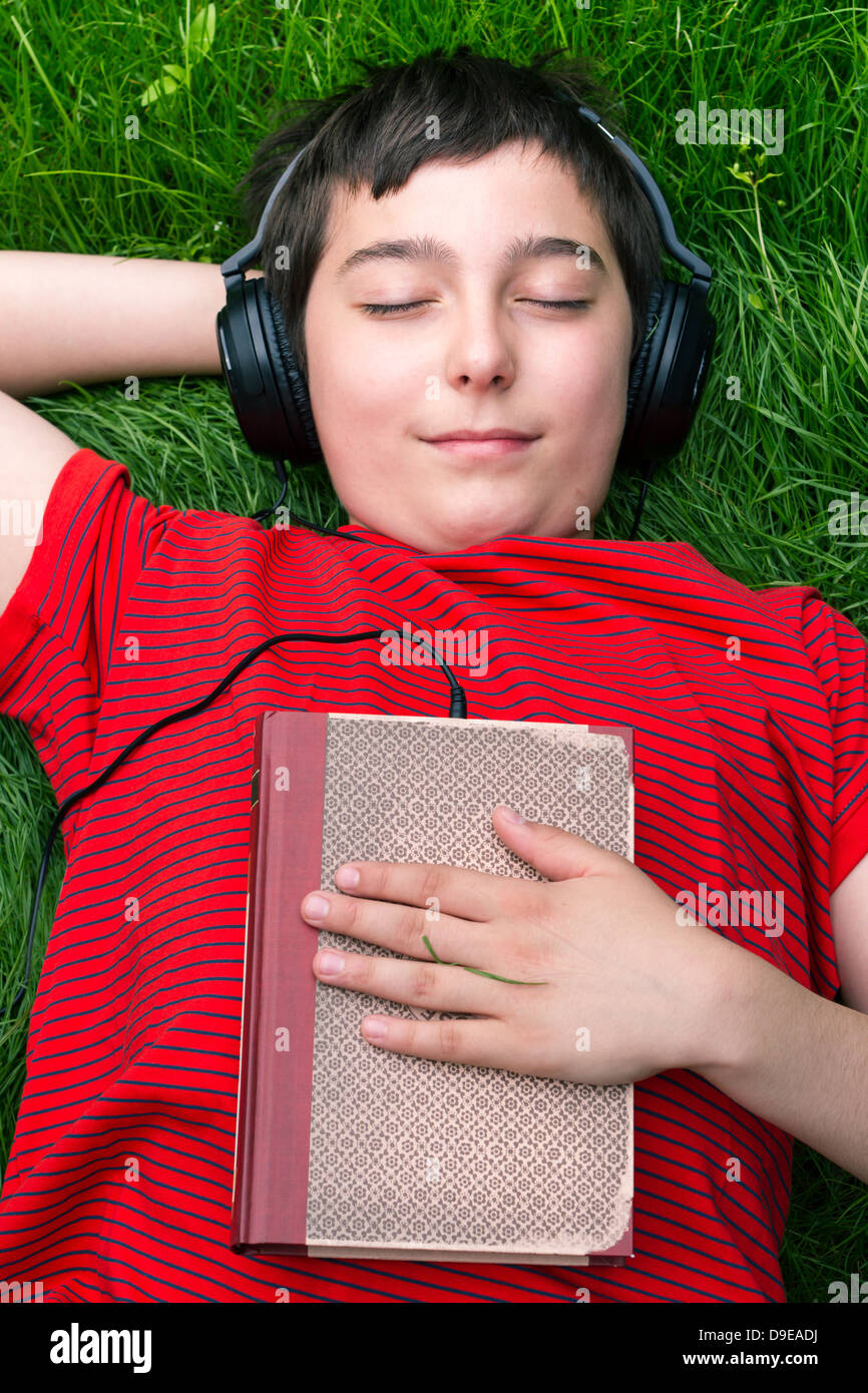 Garçon est allongé sur une herbe et il est à l'écoute de livres audio Banque D'Images