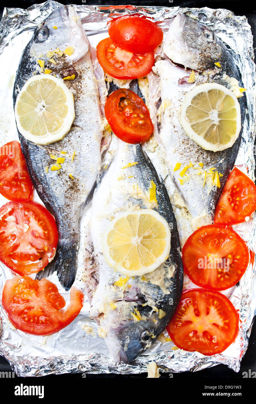 La dorade fraîche avec du citron, des tomates et des épices sur une feuille de cuisson Banque D'Images