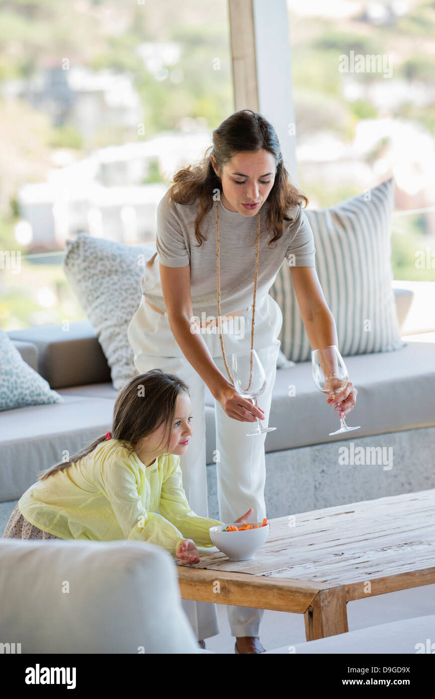Woman putting stem verres sur une table à côté de sa fille à la maison Banque D'Images
