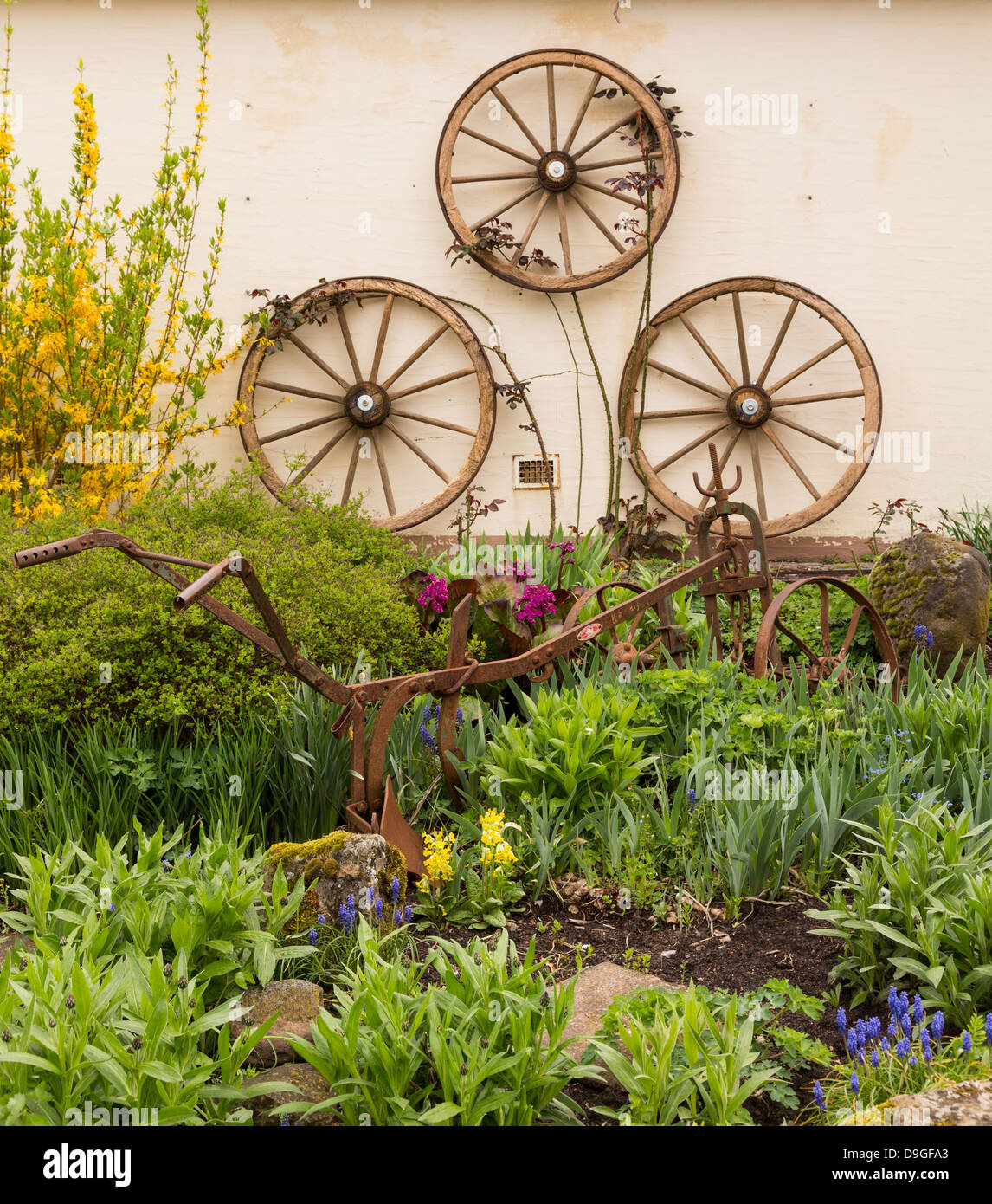 3 anciennes roues de chariot en bois fixé au mur en fer rouille rural jardin avec charrue charrue ou parmi les fleurs et plantes Banque D'Images