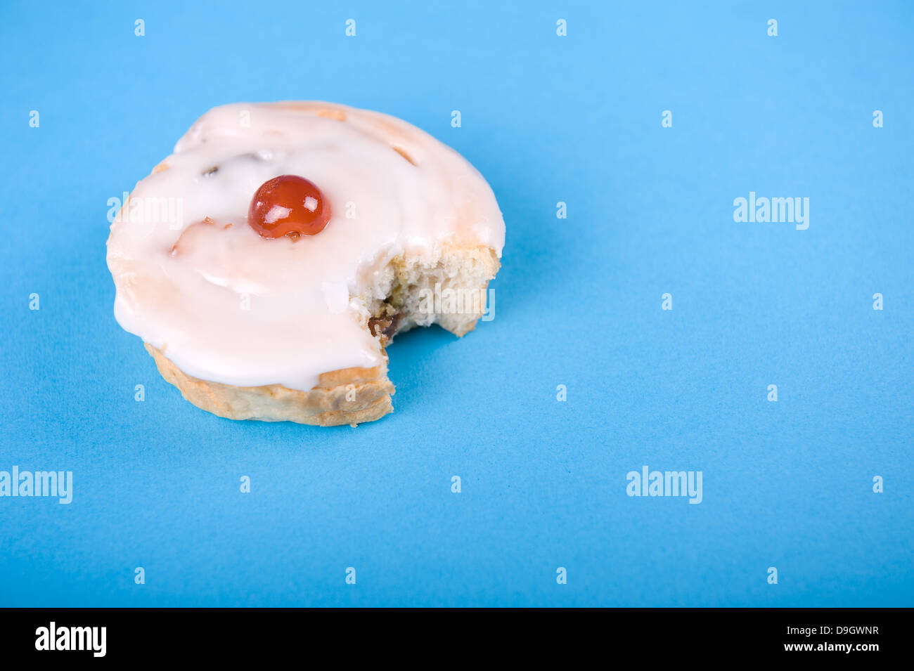 Gâteau glacé avec une cerise sur le dessus et une grande bite en elle, sur un fond bleu. Banque D'Images