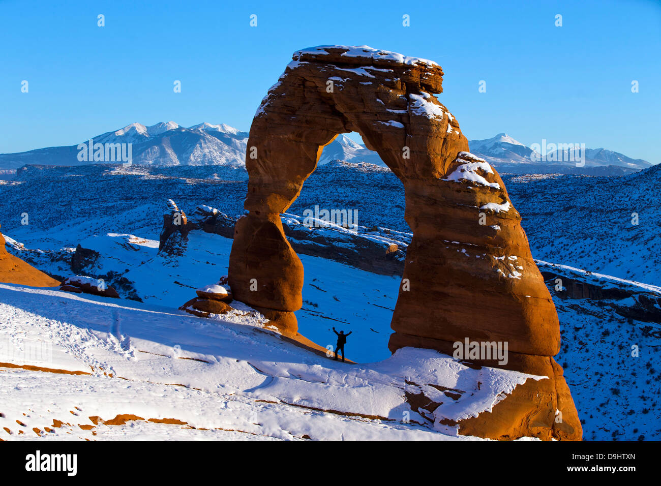Une personne se tenant debout avec les bras sous l'arche délicate avec la neige en hiver au coucher du soleil, Arches National Park, Utah, United States of America Banque D'Images