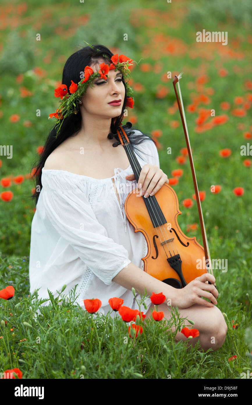 Une fille avec un violon dans une chemise blanche sur un champ de coquelicots Banque D'Images