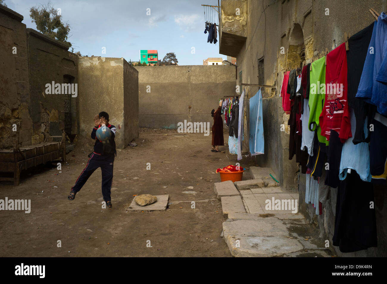 Les garçons jouent au football dans la rue tandis qu'une femme se bloque sur une ligne de lavage à sec dans le Nord de la zone du cimetière, Le Caire Égypte Banque D'Images