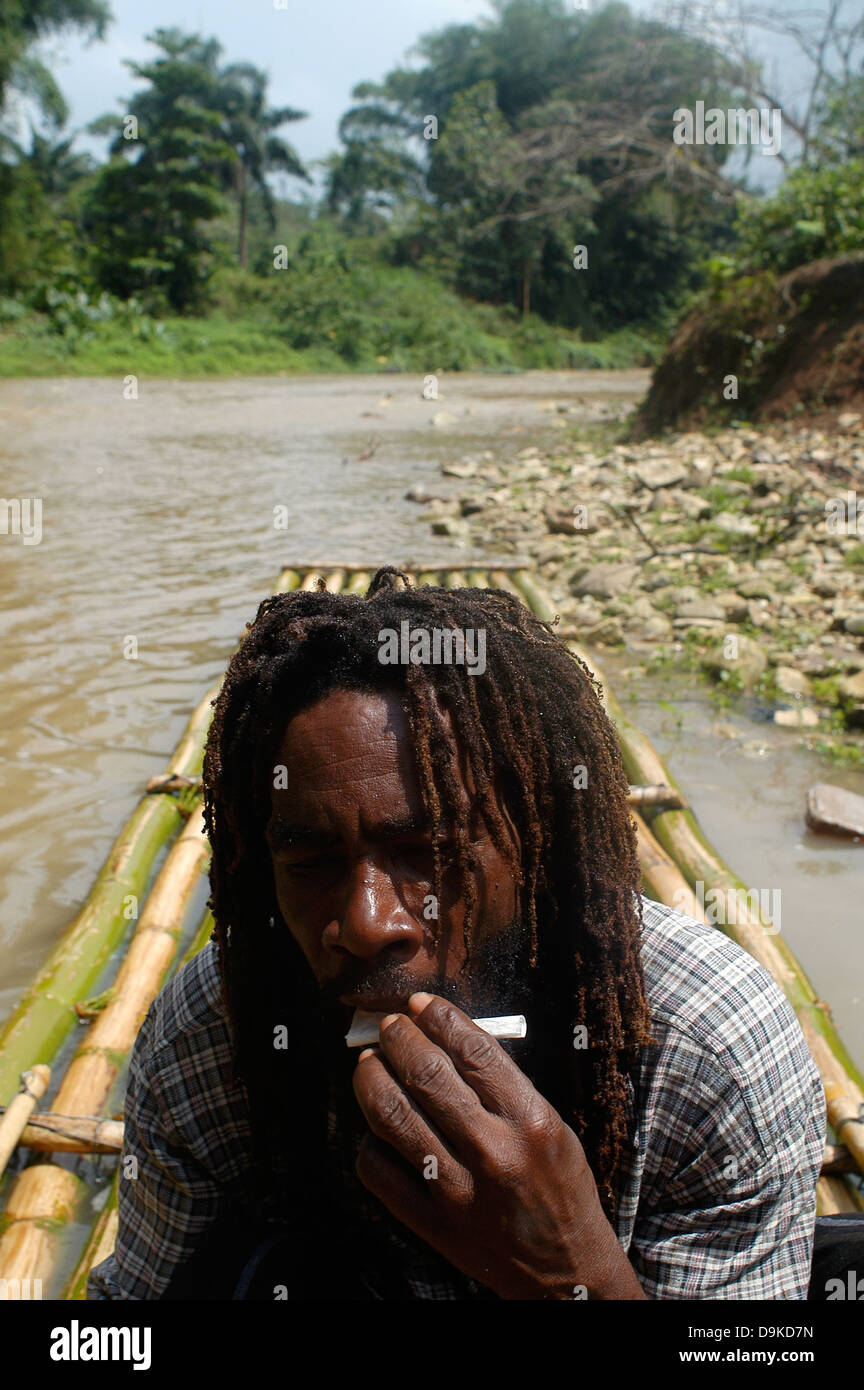 Rasta Man de rouler un joint de marijuana à bamboo rafting, grand fleuve, Jamaïque Banque D'Images