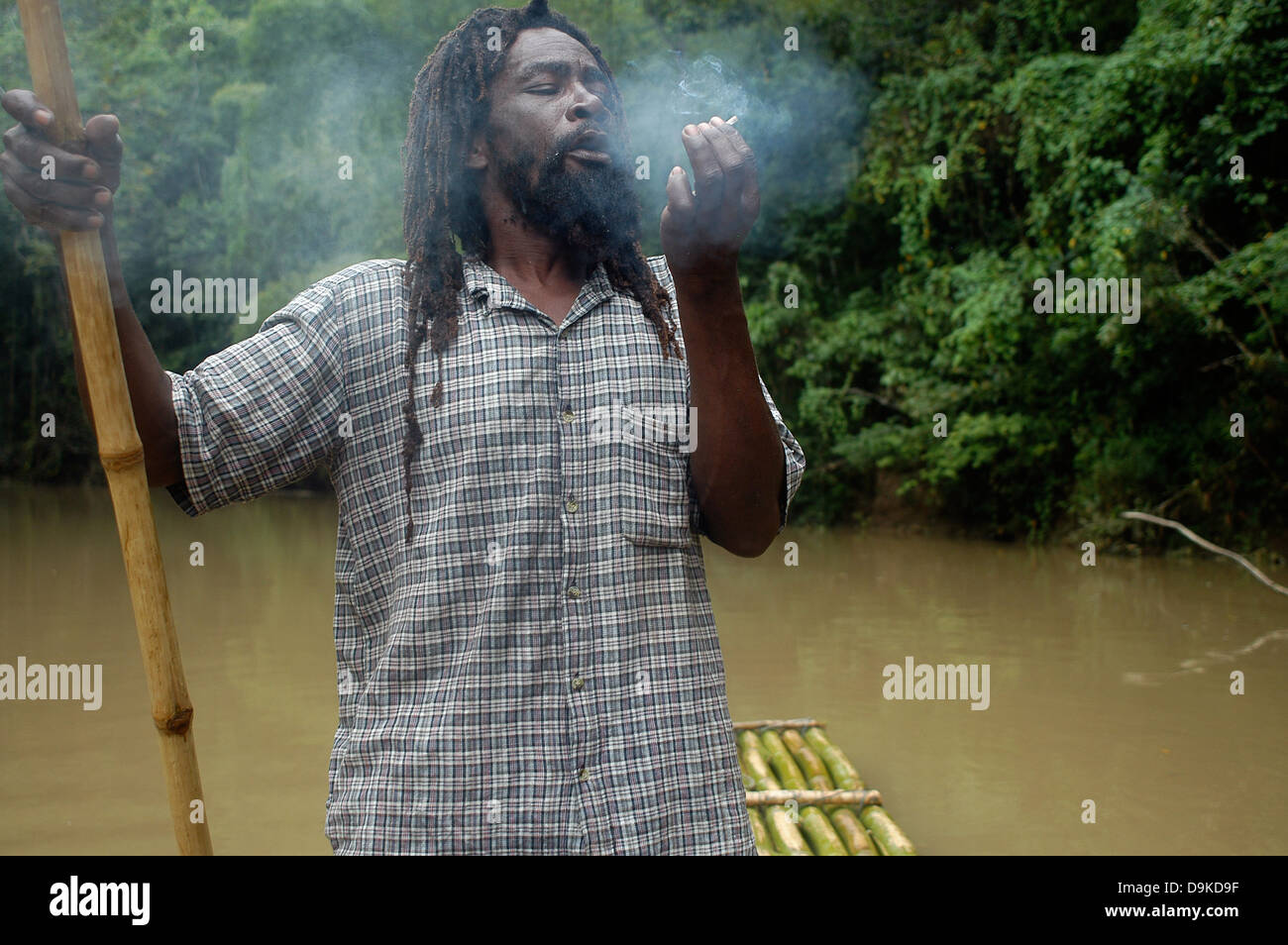 Rasta Man smoking a cigarette de marijuana à bamboo rafting, grand fleuve, Jamaïque Banque D'Images