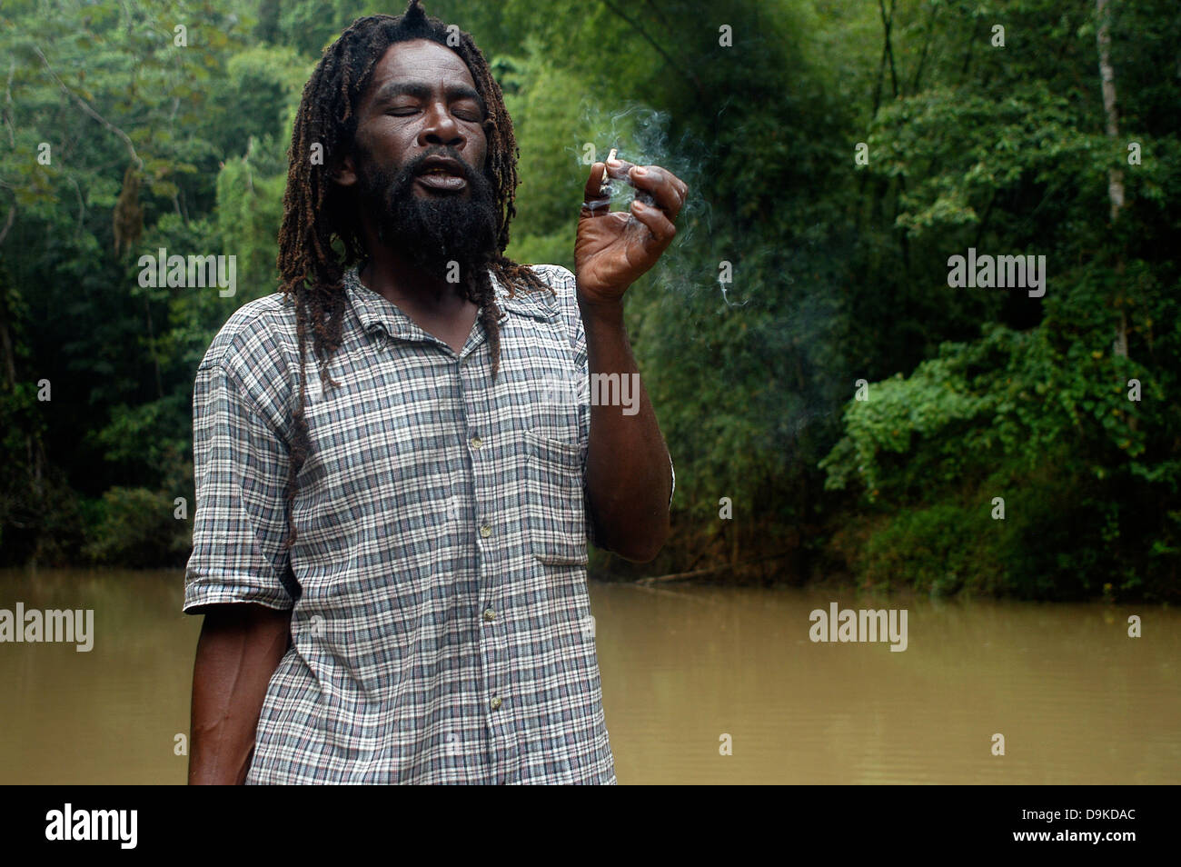 Rasta Man smoking a cigarette de marijuana à bamboo rafting, grand fleuve, Jamaïque Banque D'Images