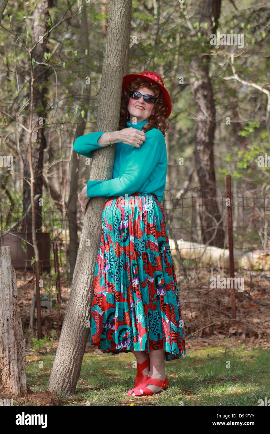 Femme en robe colorée et red hat étreindre un arbre Banque D'Images