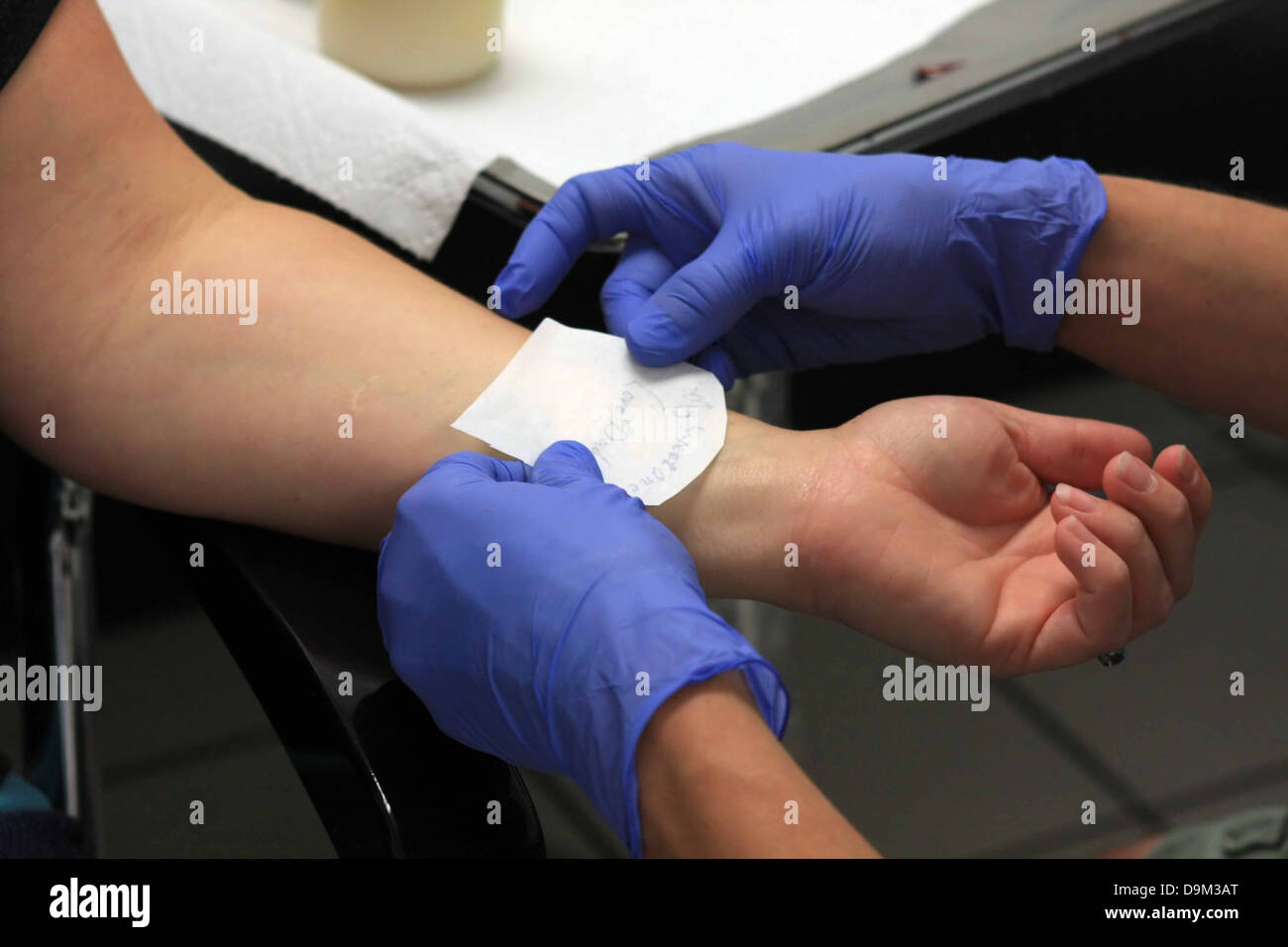 Personne en préparation avec pochoir pour obtenir un tatouage sur le poignet gauche, l'artiste portant des gants bleu Banque D'Images