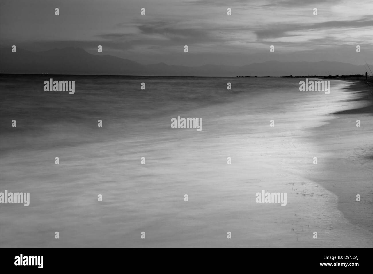 Un bel après-midi / paysage paysage marin avec un ciel calme , vagues , et un pêcheur dans la distance en B&W Banque D'Images