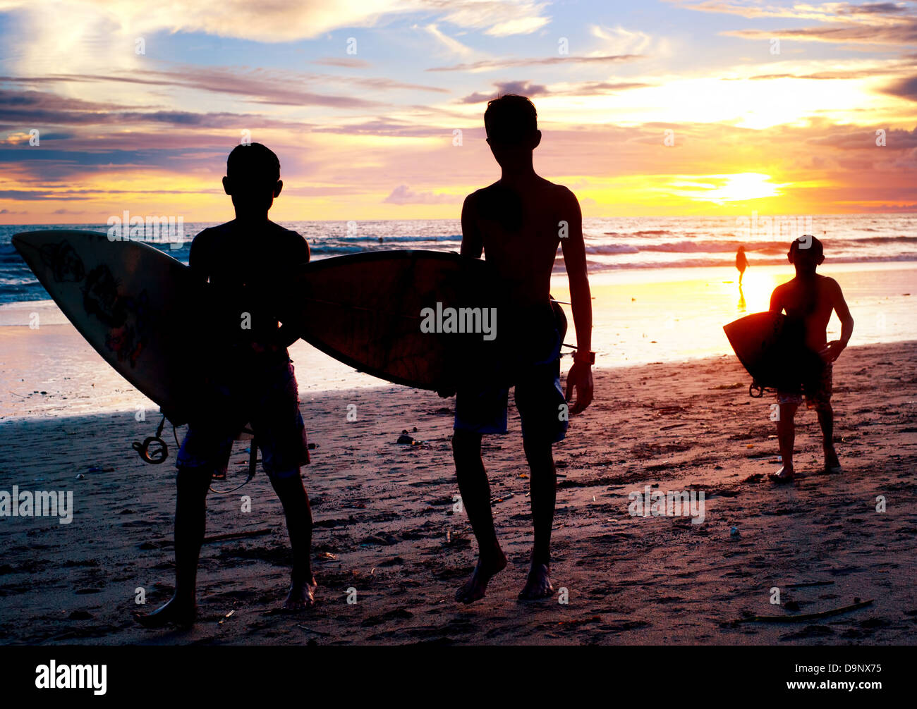Les garçons locaux avec un surf au coucher du soleil sur la plage. Bali, Indonésie Banque D'Images
