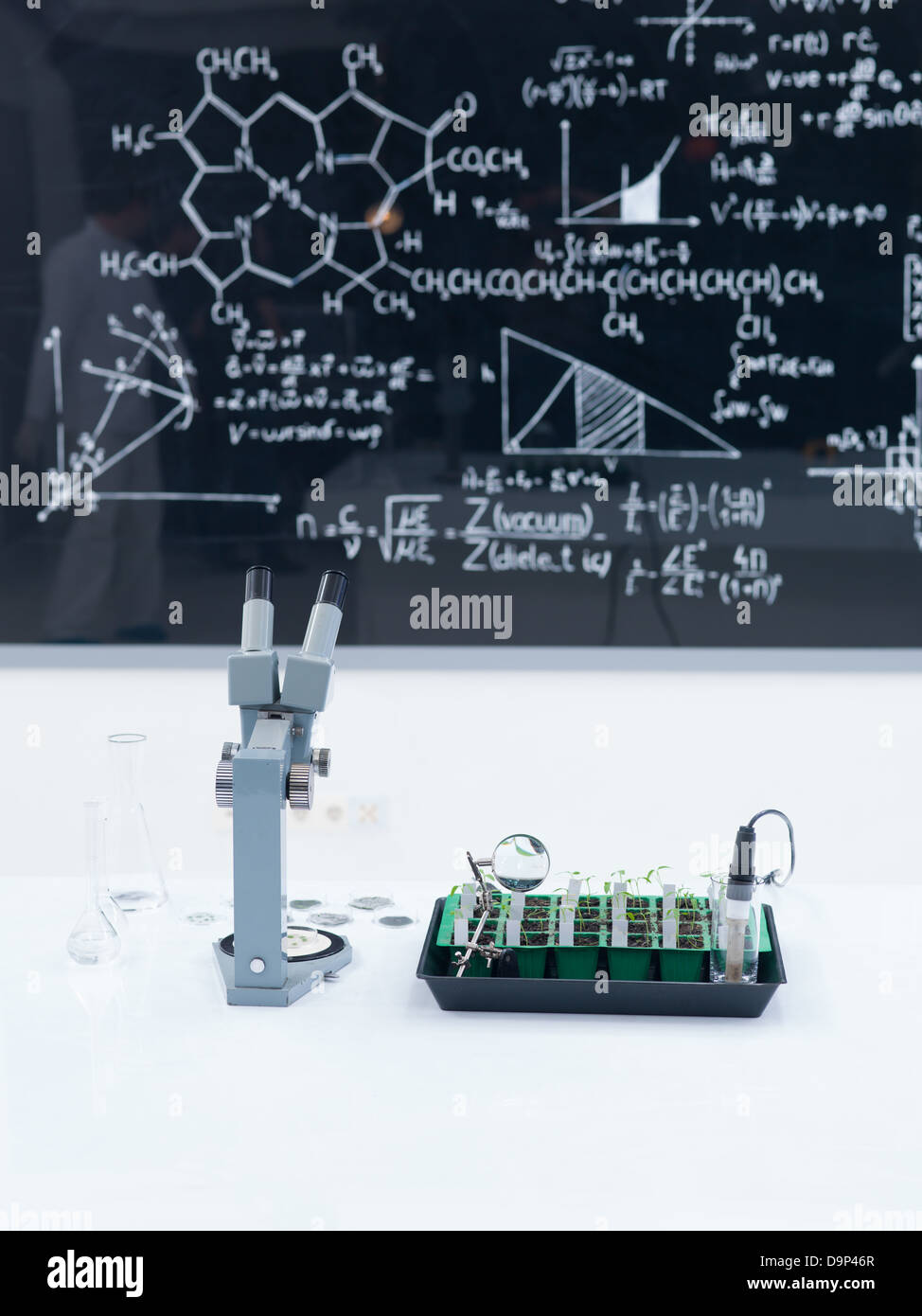 Close-up d'une table de travail de laboratoire avec des semis et d'un microscope sur elle et un tableau noir avec des formules sur l'arrière-plan Banque D'Images