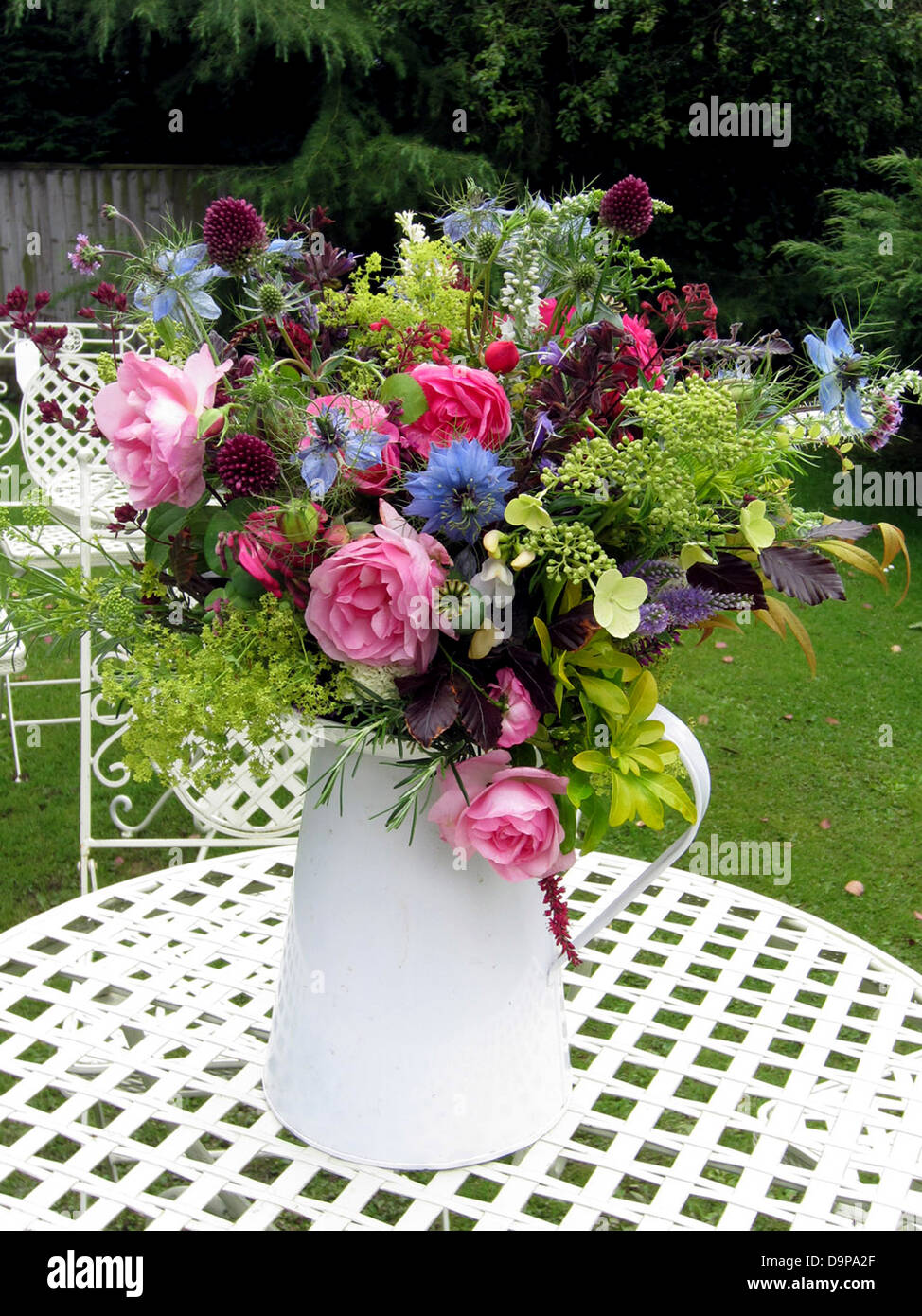 Une sélection de fleurs de jardin anglais dans un simple vase blanc dans un jardin anglais. Banque D'Images