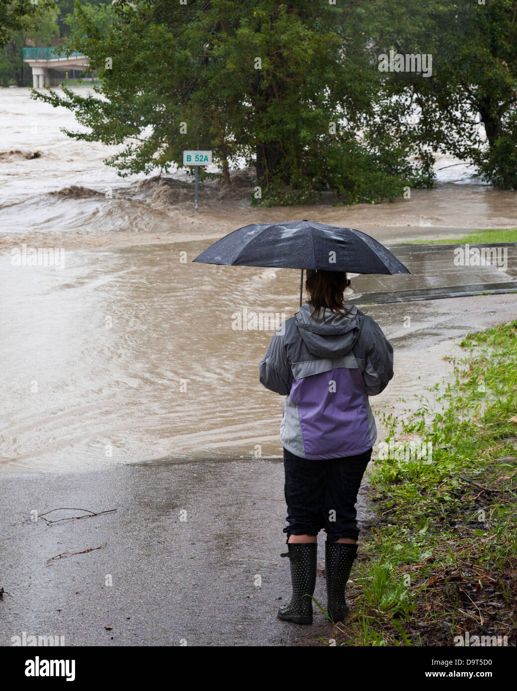Woman holding umbrella regarder la rivière Bow, à l'encontre de la Banque mondiale et d'inonder le chemin piétonnier dans le centre-ville de Calgary Banque D'Images